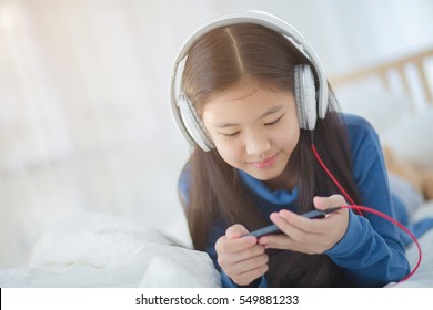 Pretty Asian Girl Using Headphone For Listen Music By Smartphone On The Bed In Her Decorated Bedroom