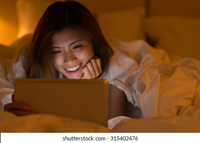 Pretty Asian girl watching movie on her tablet late at night