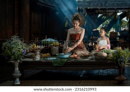 Pretty Asian girl wearing ancient native Northern Thai traditional dress costumes teaching her son to cook delicious food in the old style of Thai culture in the kitchen at an ancient wooden house.