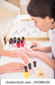 Pretty Asian Manicurist Applying Nail Polish To Client. Hands Care Concept.