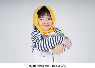 Pretty Asian Thai Kid Play Role As A Waitress Wearing Yellow Bandage Hugging Cooking Pot Isolate Over White Background.