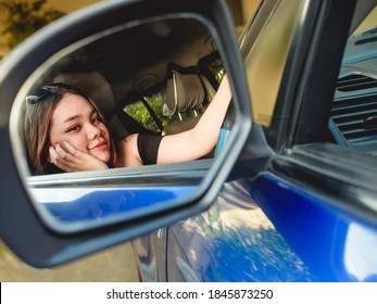 A Pretty Asian Woman Admires Herself On The Side Mirror Of Her Blue Car. Vanity Or Upbeat Feels.