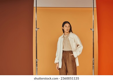 pretty asian woman in autumn outfit posing with hand in pocket, leather pants and outerwear