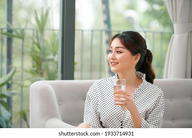 Pretty Asian Woman Drinking Water On Couch At Home In The Living Room