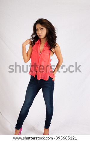 Pretty Asian woman in pink blouse and jeans, standing with a thoughtful expression and her hands in her hair