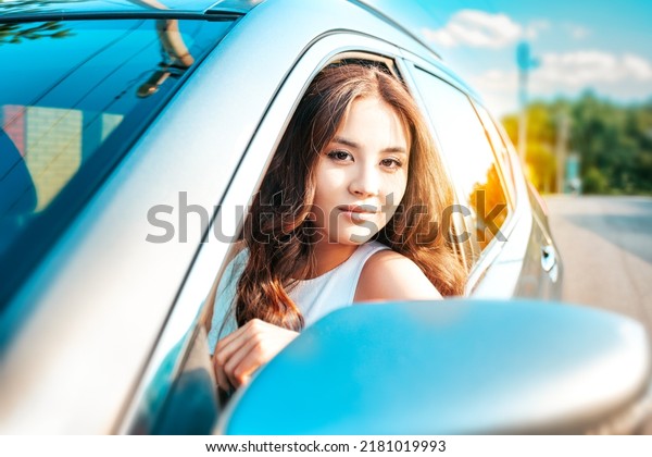 Pretty\
asian woman portrait close up. Beautiful asian girl driving her car\
and peeking out the car window and looking at\
us.