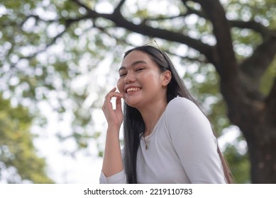 A Pretty Asian Woman Poses For The Camera With A Bright Smile On Her Face For A Low Angle Shot With Nature Background.