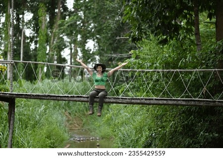 Pretty Asian woman sitting and posing at the suspension bridge over the stream in the forest which is a tourist attraction happily. Stock photo © 