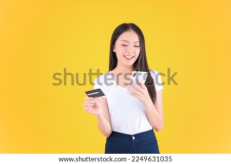 pretty asian woman smile showing, presenting credit card for payment or paying online in holding mobile phone payment credit card for confident money and financial concepts yellow background.