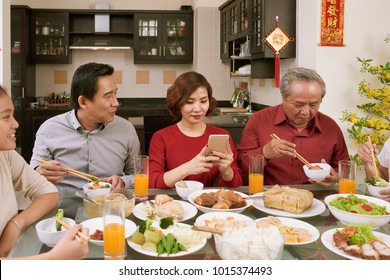 Pretty Asian woman taking photos of food at Chinese New Year celebration. Scrolls wishing luck and wealth in the background