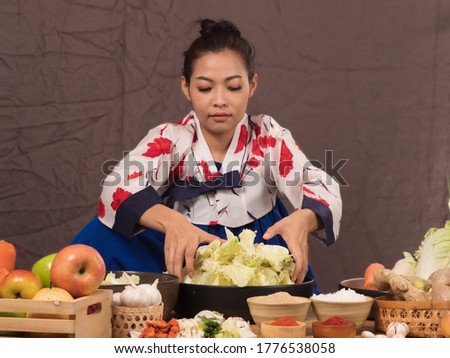 Pretty Asian woman in traditional Korean dress, Hanbok, making Kimchi, Korean cuisine side dish, fermented vegetables, using lettuce, carrots, green onion mix with chili, garlic, onion, ginger.
