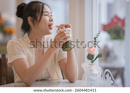 Pretty Asian woman travelers are holding a Matcha latte green tea with cold refreshing drinks, enjoying a peaceful moment of wellness to relax, wearing modern Handwoven Fabric and blue jeans.