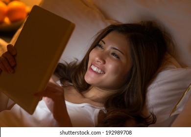 Pretty Asian woman using digital tablet in bed at night - Powered by Shutterstock