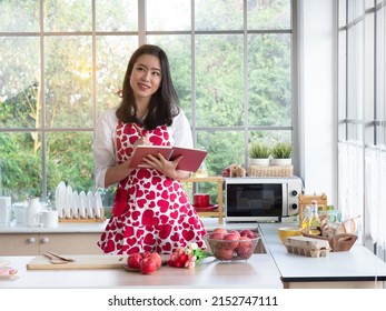 Pretty Asian woman wearing cute apron holding cook book thinking of what to cook. - Shutterstock ID 2152747111