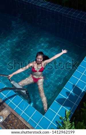 Pretty Asian woman wearing red bikini swimming on back at swimming pool and enjoying travel on vacation summer time.   