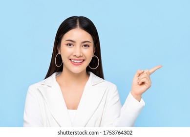 Pretty Asian woman in white suit smiling and pointing finger to space aside isolated on light blue background - Shutterstock ID 1753764302