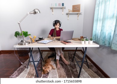 Pretty Asian Woman Working Remotely From Home Using Laptop Sitting On The Couch Or Sofa In Living Room For Work Online With Pet Puppy Cute Dog And Guardian, Work Life Balance Concept
