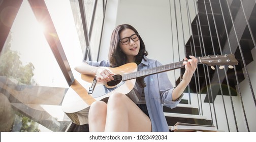 Pretty asian young girl playing some record on guitar near the window. Asian woman's hands playing acoustic guitar, close up vintage. Education lifestyle relax concept  - Powered by Shutterstock