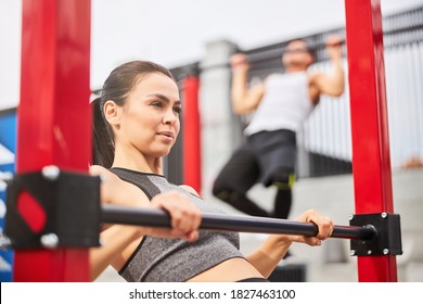 Pretty athletic female and strong male are exercising and doing pull ups on horizontal bars in open air - Powered by Shutterstock