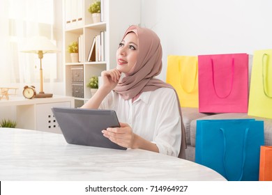 Pretty Attractive Muslim Woman Looking At Air Daydreaming Thinking When She Using Mobile Pad Computer Online Shopping At Home.