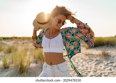 pretty attractive slim smiling woman on sunny beach in summer style fashion trend outfit happy, freedom, wearing white top, jeans and colorful printed tunic boho style chic and straw hat - Powered by Shutterstock