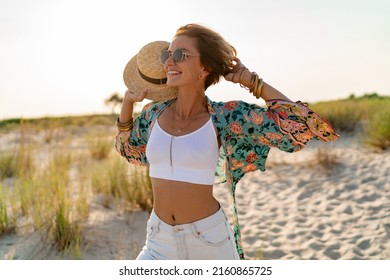 pretty attractive slim smiling woman on sunny beach in summer style fashion trend outfit happy, freedom, wearing white top, jeans and colorful printed tunic boho style chic and straw hat - Powered by Shutterstock