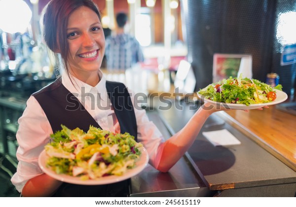 バーにサラダの皿を持つきれいなバーメイド の写真素材 今すぐ編集