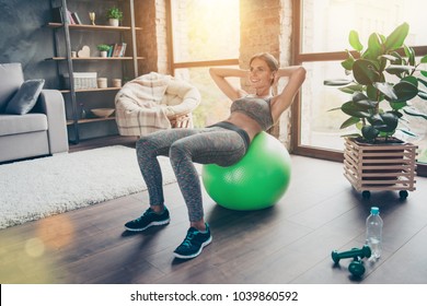 Pretty Beautiful Powerful Skinny Cheerful Woman Clothed In Sportive Outfit Lying On Green Fit Ball And Doing Crunches At Home In Sun Beam, Light, Glare, Sunny Day, Reflection