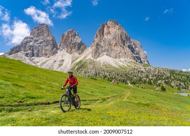 pretty beautiful senior woman riding her electric mountain bike below famous Sassolungo summit in Sella Dolomites  of Selva Wolkenstein, Val Gardena, South Tirol and Trentino, Italy