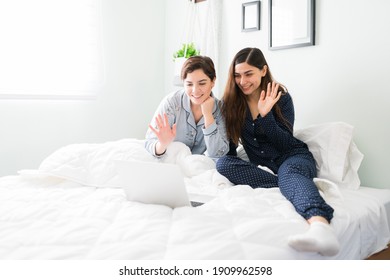 Pretty Best Friends Saying Hello An Talking To Friends During An Online Video Call In A Laptop. Two Women Having A Video Chat With Their Family In Bed 