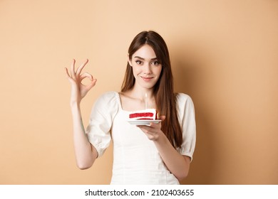 Pretty Birthday Girl Holding Cake And Showing OK Gesture, Smiling Pleased, Enjoying Bday Celebration, Beige Background