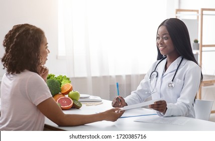 Pretty black doctor dietician giving female patient treatment plan, consultation at clinic, copy space