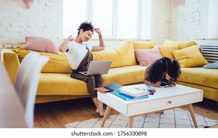 Pretty black lady sitting with laptop in cozy room and stretching arms during break while little girl leaning over tablet - Powered by Shutterstock