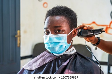 Pretty Black Lady Wearing Surgical Face Mask In A Hair Salon Or Barber Shop In Covid-19 Pandemic With Hair Clipper Behind Her Hair