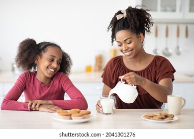 Pretty black mother pouring fresh milk for her teen daughter, happy afro-american girl having breakfast with her loving mom, kitchen interior. Healthy diet, calcium, vitamins in kids food concept - Powered by Shutterstock