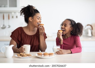 Pretty Black Mother And Teen Daughter Eating Cookies, Happy African American Girl Having Breakfast With Her Loving Mom, Kitchen Interior. Healthy Diet, Calcium, Vitamins In Kids Food Concept