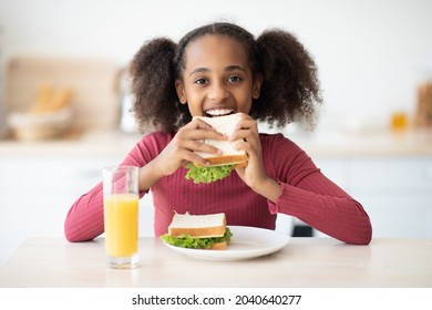 Pretty Black Teen Girl With Bushy Curly Hair Having Snack At Home, Eating Vegetable And Greens Sandwich, Drinking Fresh Orange Juice, Closeup Portrait. Healthy Lifestyle, Diet For Teenagers, Kids