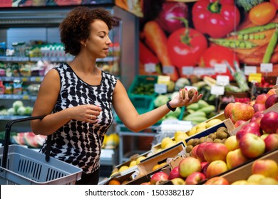 Hübsche schwarze Frau, die in einem Lebensmittelgeschäft Obst auswählt