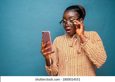 Pretty Black Woman Pulling Down Spectacles To A Surprise On Phone With Ear Piece In Her Ear-concept On Technology And Lifestyle