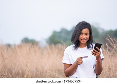 Pretty Black Woman Smiling While Using Her Credit And Phone, Paying Online And Shopping Concept, Looking At The Camera