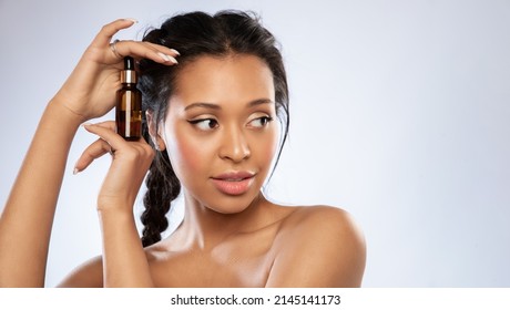 Pretty Black Young Woman Holding Bottle With Cosmetics Moisturizing Serum Or Oil, Facial Essence. Female With Bare Shoulders Showing Product For Cosmetology Beauty Skincare Routine Procedure.