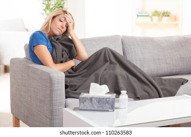 Pretty blond white female sitting on couch with a cold with gray blanket.