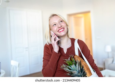 Pretty Blond Woman Arriving Home Carrying Groceries In A Eco Friendly Tote Bag Using Her Smart Mobile Phone - Multi Tasking