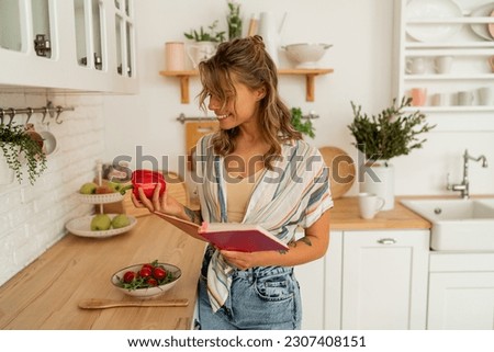 Pretty blond woman housewife browses a recipe book, making a vegetable salad in a bright kitchen. Embracing a healthy lifestyle and dieting.