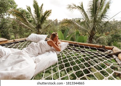 Pretty blond woman lie on hammock under the sheets on luxury bamboo eco resort with jungle nature view. Vaction on Bali island