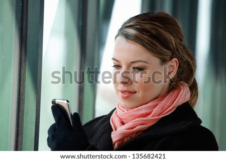 Pretty Blond Young Business Woman Using A Smartphone Wearing A Winter Coat Scarf And Gloves