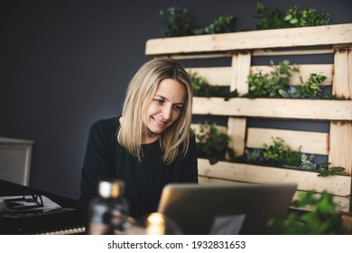 pretty blond young woman is sitting in an ecological office with lots of plants and is working on her laptop and is wearing a green sweater, concept sustainability and environment