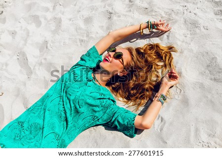 Pretty blonde girl lying on the tropical  sunny beach . Wearing cool stylish sunglasses, color    bo ho tunic and bright trendy accessories . Warm colors.