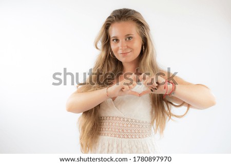 Pretty blonde girl in a white dress making heart figure with her hands