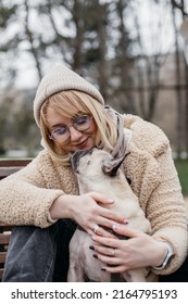 Pretty blonde hugging her cute pug. Beautiful young woman sitting outdoors with her pet in her hands.